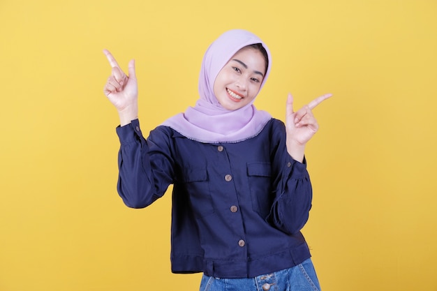 Portrait of cute woman pointing up in casual cloth wearing hijab on isolated yellow background