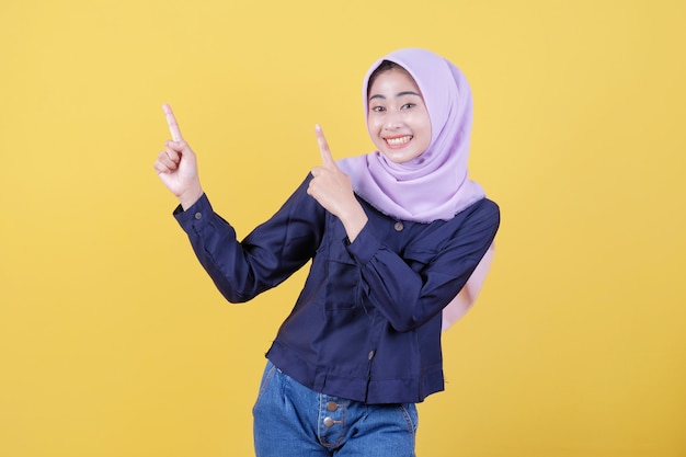 Portrait of cute woman pointing up in casual cloth wearing hijab on isolated yellow background