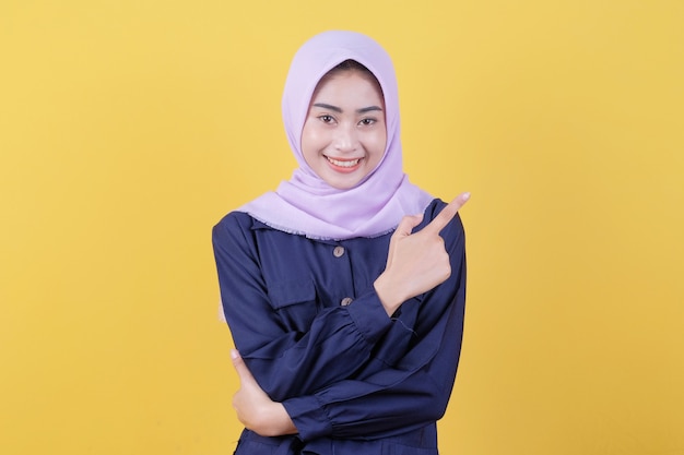 Portrait of cute woman pointing up in casual cloth wearing hijab on isolated yellow background