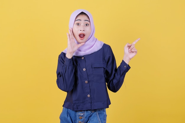 Portrait of cute woman pointing up in casual cloth wearing hijab on isolated yellow background