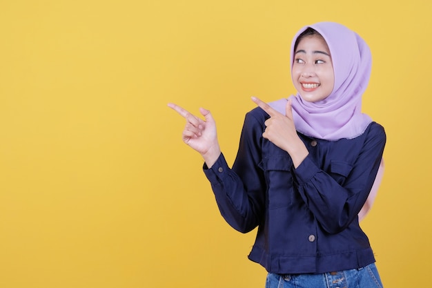 Portrait of cute woman pointing up in casual cloth wearing hijab on isolated yellow background