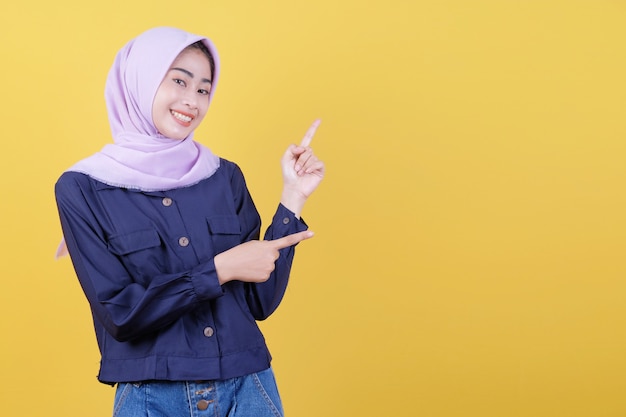 Portrait of cute woman pointing up in casual cloth wearing hijab on isolated yellow background