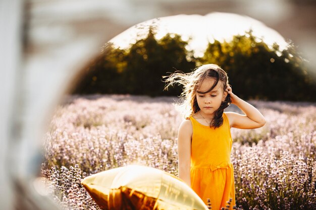 Photo portrait of a cute young girl looking thoughtfully down playing with hand in hair while being in a lavender field against sunset.