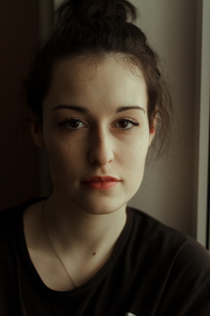 Portrait of a cute young woman with big brown eyes and freckles. Dark hair gathered in a bun. White skin. Beautiful.