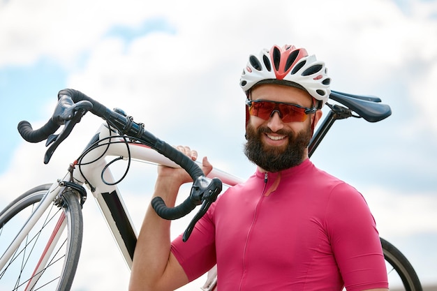 Portrait of a cyclist standing under a bridge with a bicycle in his hand posing at the camera against an architecture background Active lifestyle Cycling is a hobby