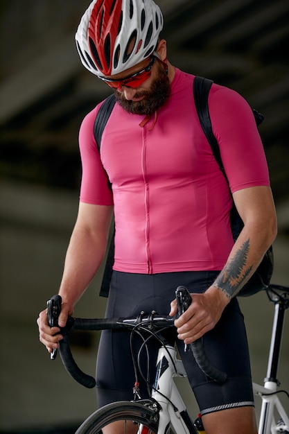 Portrait of a cyclist standing under a bridge with a bicycle in his hand posing at the camera against an architecture background Active lifestyle Cycling is a hobby