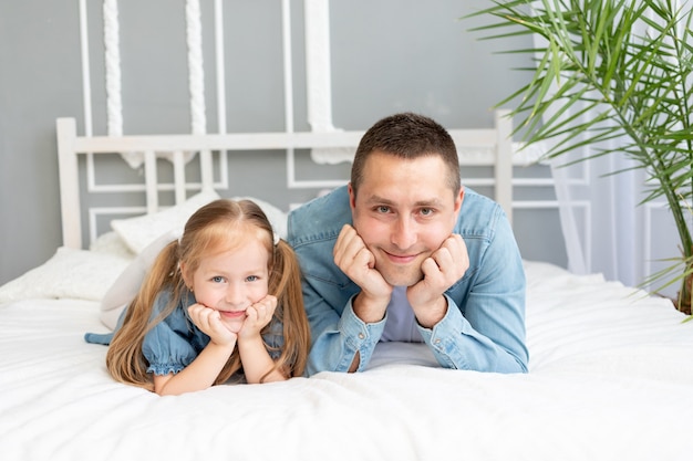 Portrait of a dad with a baby daughter having fun on the bed at home