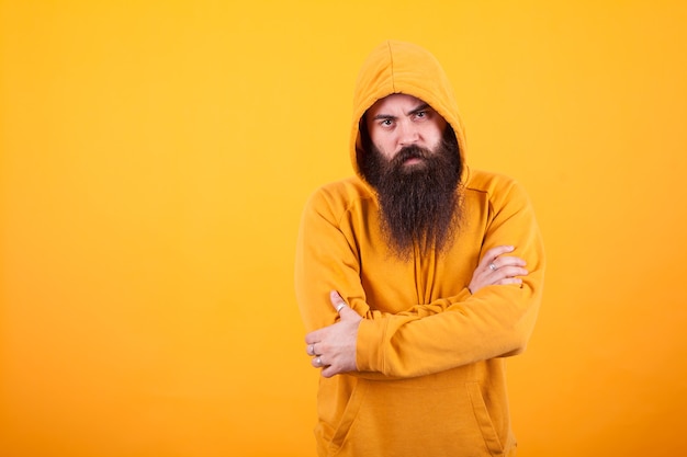 Portrait of dangerous man with long beard wearing a hoodie over yellow background. Handsome man. Stylish man.