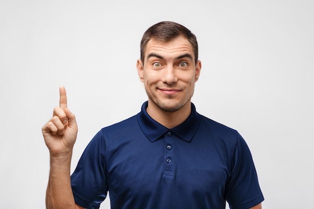 Portrait of dark haired man in blue Tshirt shows finger up on white background