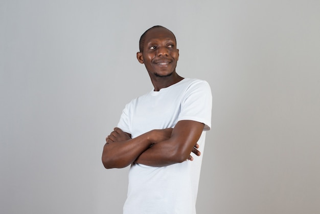 Portrait of dark skinned man in white t-shirt standing arms crossed on gray wall