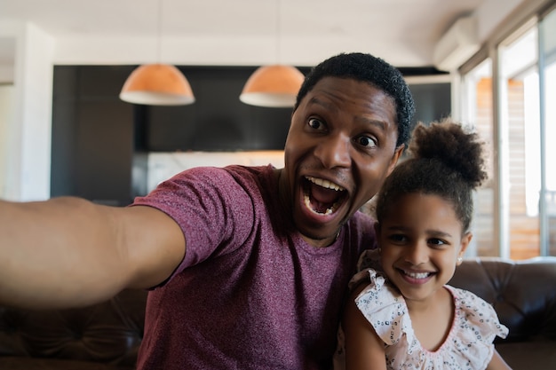 Portrait of a daughter and father having fun together and taking a selfie while sitting on couch at home