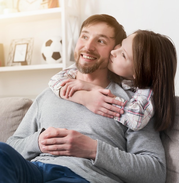 Portrait of daughter hugging and kissing happy father in cheek at home