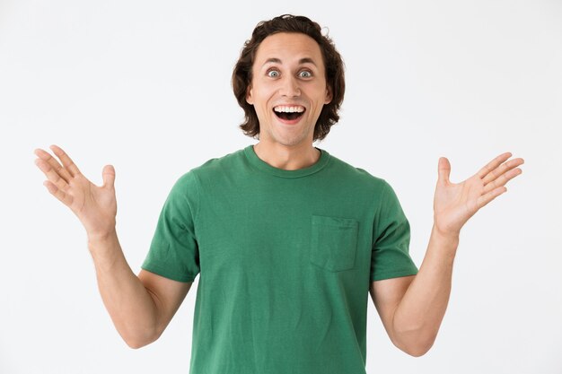 Photo portrait of delighted young man wearing basic t-shirt laughing and gesturing in wonder isolated over white wall