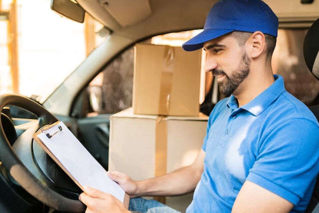 Portrait of a delivery man checking the delivery list while sitting in van. Delivery and shipping concept.