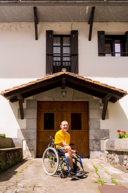 Portrait of a disabled person dressed in yellow in a wheelchair in the entrance of his house smiling