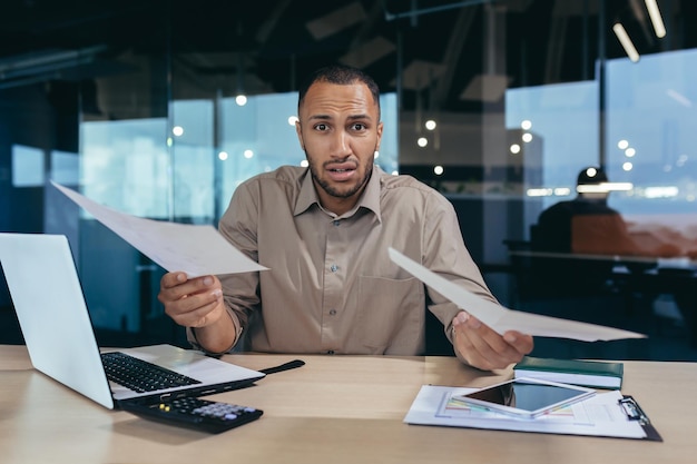 Portrait of disappointed young hispanic financier businessman looking at camera in despair and