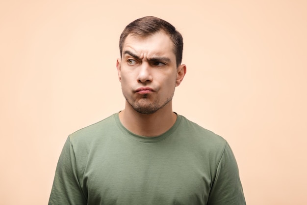 Portrait of disgruntled man with pouting lips in green Tshirt on beige background copy space