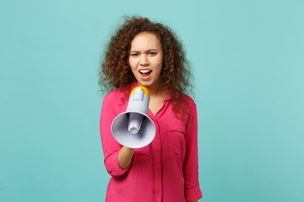 Portrait of displeased african girl in pink casual clothes scream in megaphone isolated on blue turquoise wall background in studio. People sincere emotions, lifestyle concept. Mock up copy space.