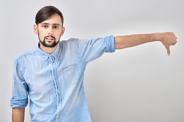 Portrait of displeased caucasian man showing thumbs down isolated on white studio background Does not approve of something puts a dislikexA