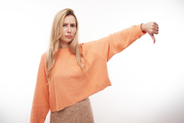 Portrait of displeased young blond woman showing thumbs down isolated on white studio background Does not approve of something puts a dislikexA