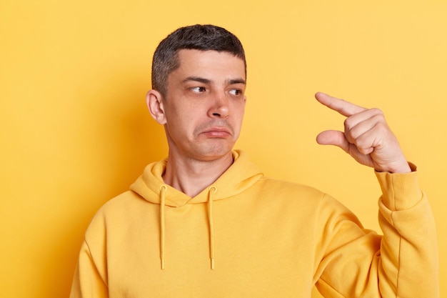 Portrait of dissatisfied man wearing casual style hoodie posing isolated over yellow background showing little size gesture with disappointed frustrated face expression