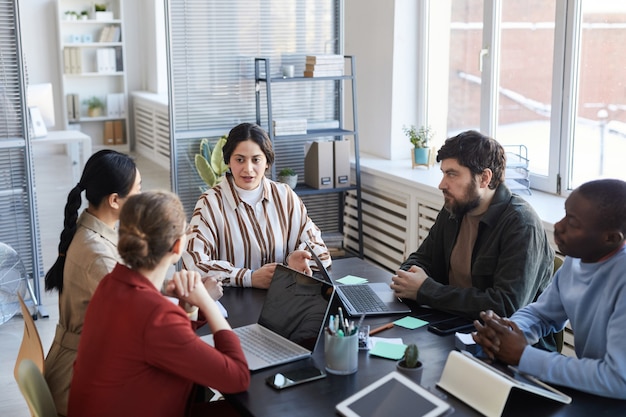 Portrait of diverse group of business people at table collaborating during briefing meeting in office, focus on Middle-Eastern female manager