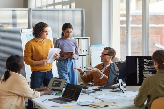 Portrait of diverse software development team collaborating on project in modern office, focus on lead engineer instructing colleagues, copy space