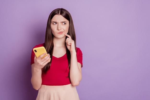 Portrait of dobtful jealous minded lady hold phone look blank space think on violet background