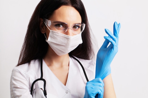 Portrait of a doctor in glasses and a white medical gown wearing personal protective equipment.