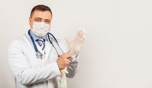 Portrait of a doctor in medical mask and lab coat putting on sterile gloves