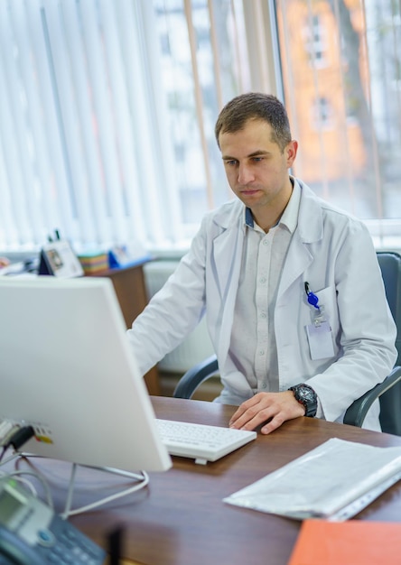 Portrait of a doctor or medical specialist. Office background. Male medic is working on computer. Closeup.