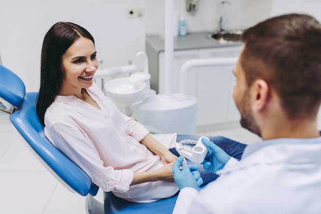 Portrait of doctor and patient looking at jaws model in modern dental clinic