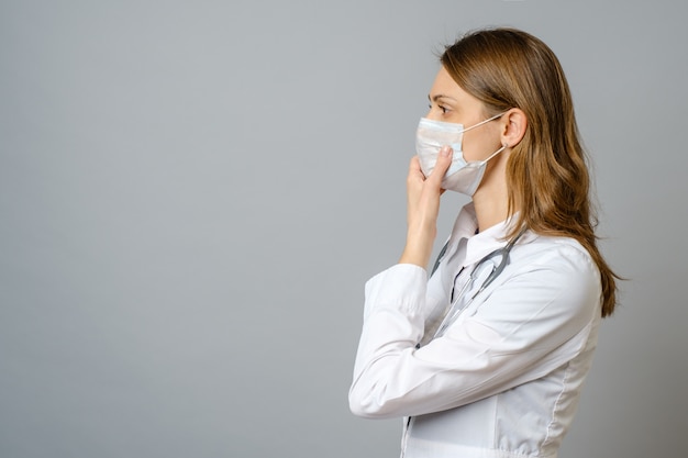 Portrait of doctor putting sterile mask isolated on gray