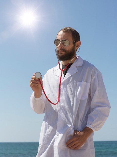 Portrait of doctor with stethoscope in ear listen you carefully attentively. American handsome bearded man on blue sky background. Russian Caucasian brutal man in a white coat. Treatment in Israel