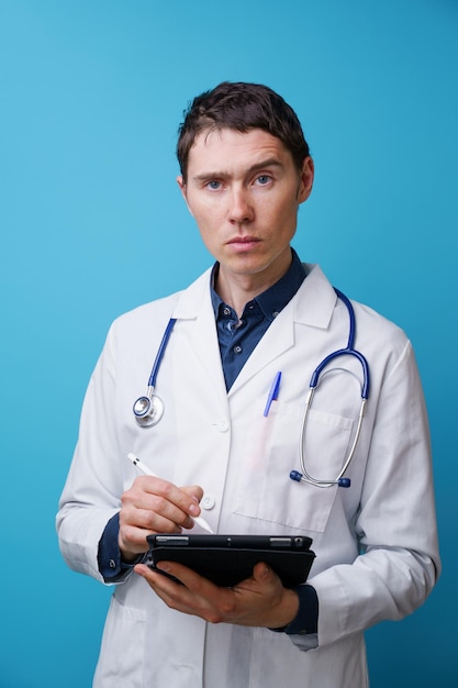 Portrait of doctor with stethoscope and tablet computer in hand on blue background