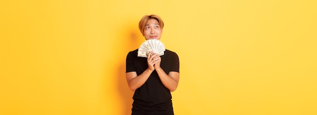 Portrait of dreamy handsome asian guy showing his savings and thinking looking upper left corner hol