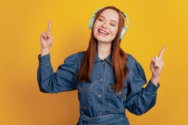 Portrait of dreamy inspired lady wear earphones listen music raise fingers on yellow background