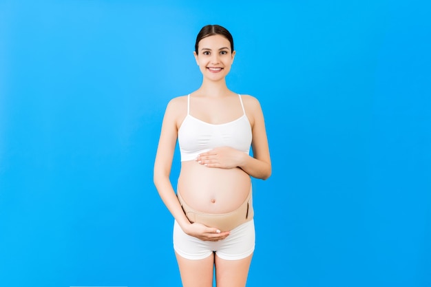 Portrait of elastic maternity band dressed on pregnant woman in underwear to reduce backache at blue surface with copy space