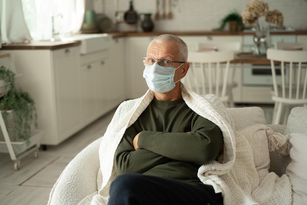 Portrait of an elderly grayhaired man in a protective face mask in a cold winter at home