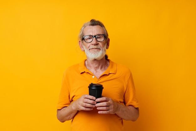 Portrait elderly man with black disposable cup yellow background