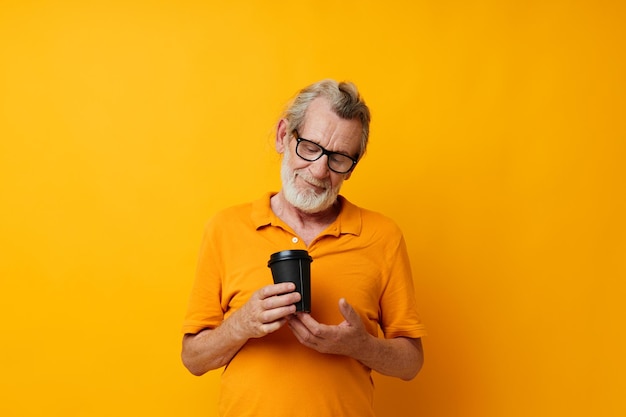 Portrait elderly man in a yellow Tshirt a glass with a drink yellow background