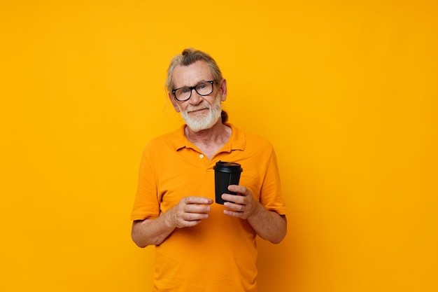 Portrait elderly man in a yellow Tshirt a glass with a drink yellow background