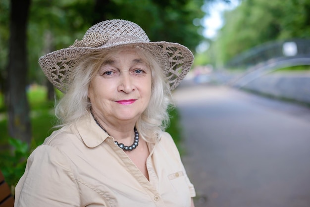 Portrait of an elderly woman with gray hair in a hat and beige dress in the park