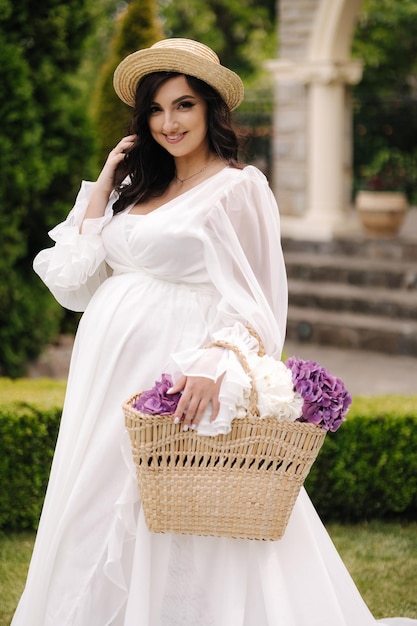 Portrait of elegant pregnant woman in beautiful white dress walking outdoors future mom hold wicker