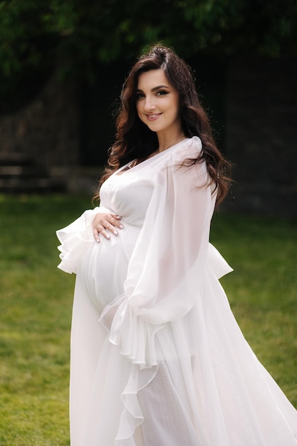 Portrait of elegant pregnant woman in beautiful white dress walking outdoors