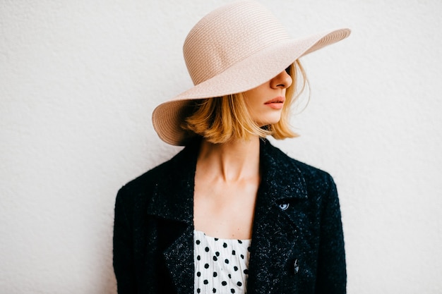 Portrait of elegant stylish blonde short hair girl in hat and jacket posing over white