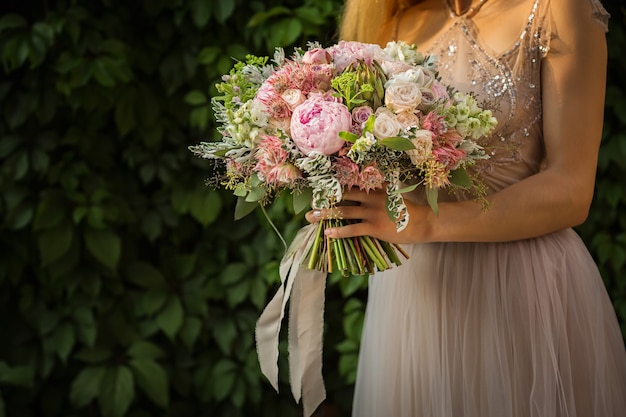 Portrait of an elegant unrecognizable pretty woman wearing grey wedding dress and posing in the street. Bride holds a bouquet of pastel flowers and greenery