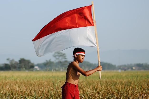 Portrait of elementary school boy on the rice field flapping an Indonesian flag celebrating independ