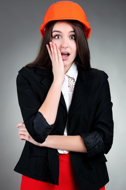 Portrait of emotional girl in construction helmet on gray