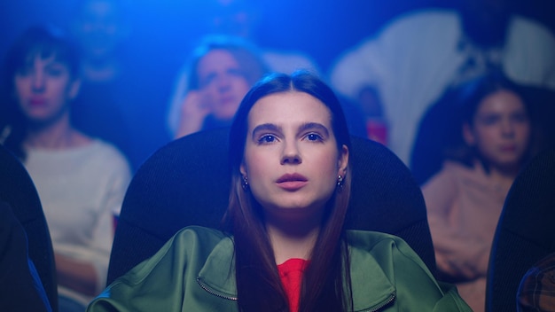 Portrait of emotional woman sitting in dark hall during sentimental film Closeup worried girl watching romantic moments of melodrama in cinema Beautiful lady spending evening in movie theater